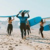 People Running on Beach with Surfboards